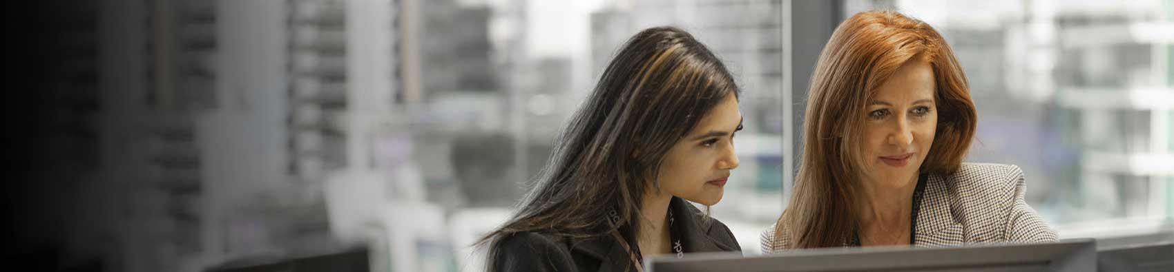 Two people in an office standing at a desk and look at a monitor