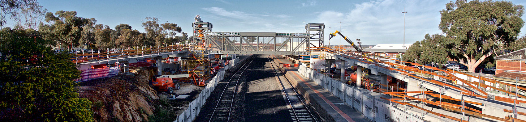 Railway tracks near a train station. An overpass is being built and there is construction works taking place on both sides of the tracks.