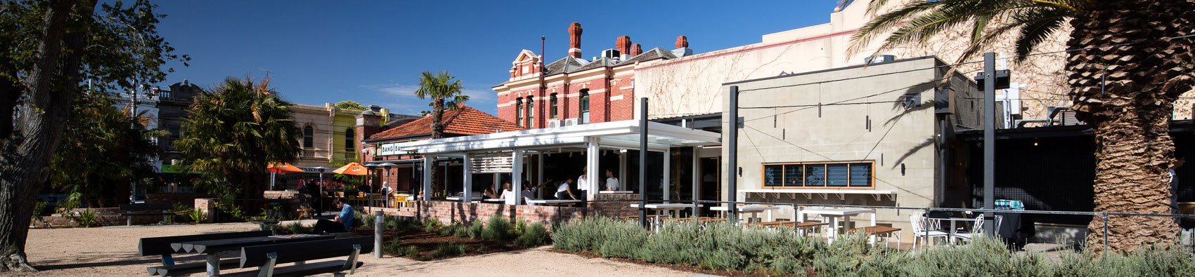 A view of the upgraded precinct at Glenhuntly Station. It shows Bang Bang Bar in the background with outdoor seating. There are trees on either side.