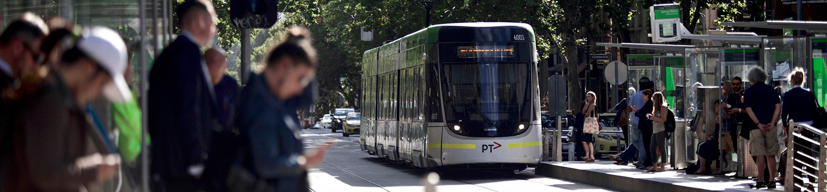 A city tram stop with platforms on both sides of the street. Passengers are waiting on the platforms. A tram is approaching one platform.