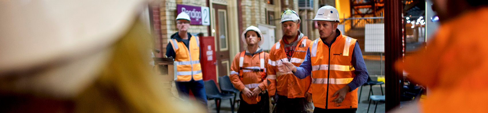 A group of workers in safety hi vis and helmets standing at at train station.