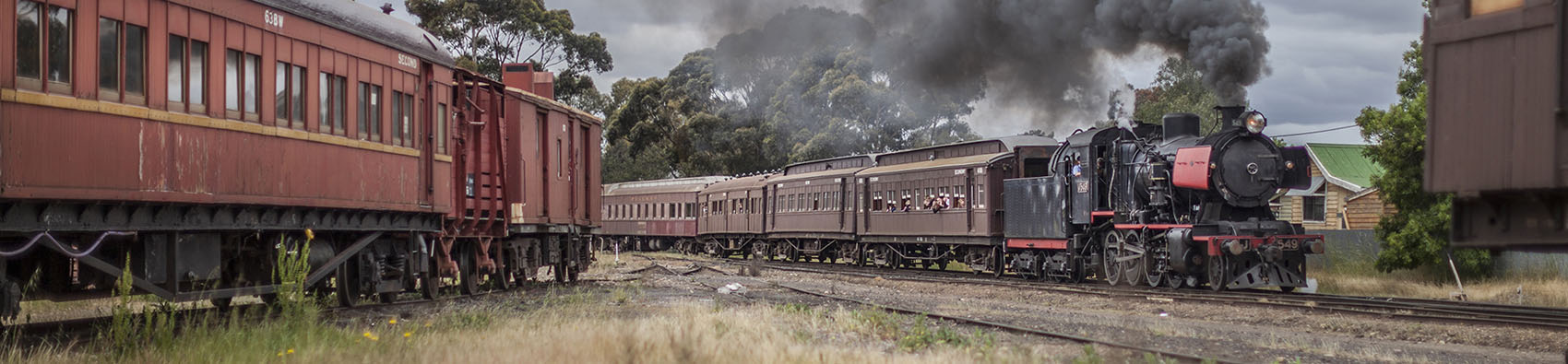 An operational steam track billowing black smoke. On one side is a stationary vintage train.