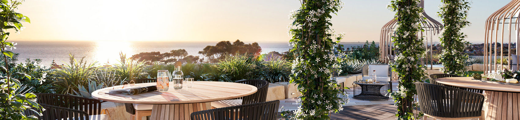 An outdoor dining area with tables, chairs, and plants overlooking the sea.