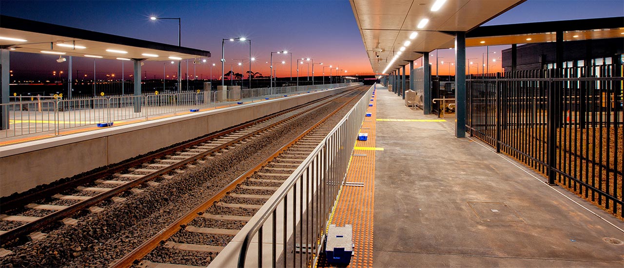 A new train station in the evening time from the platform point of view. The evening shows a blue and orange sky as the sun sets.