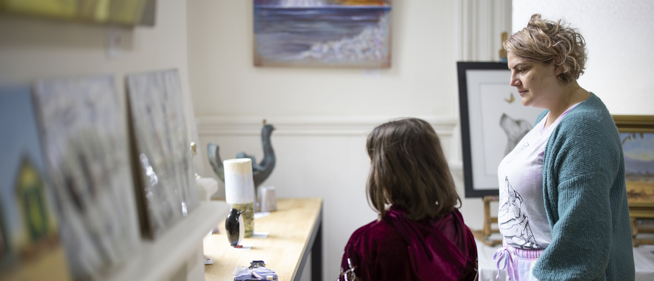Two people look at paintings and small sculptures in an art gallery housed in a railway building