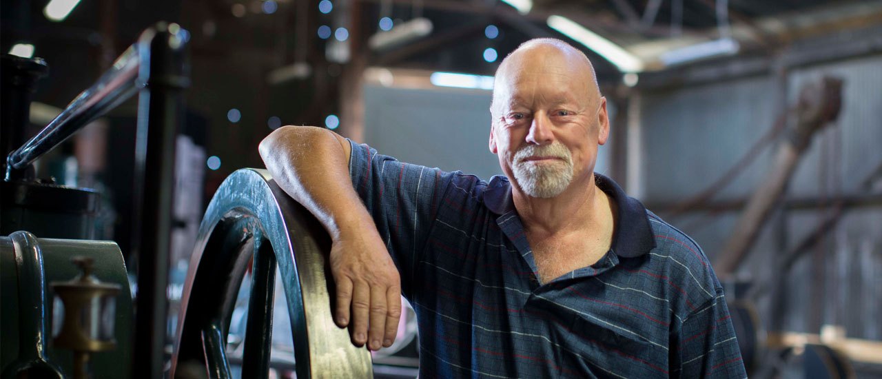 A person leans on the wheel of heritage railway equipment in a goods shed while looking towards the camera.