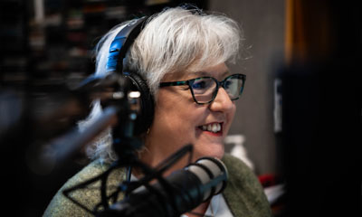 Image of a radio presenter in the radio studio. Wearing headphones and smiling.